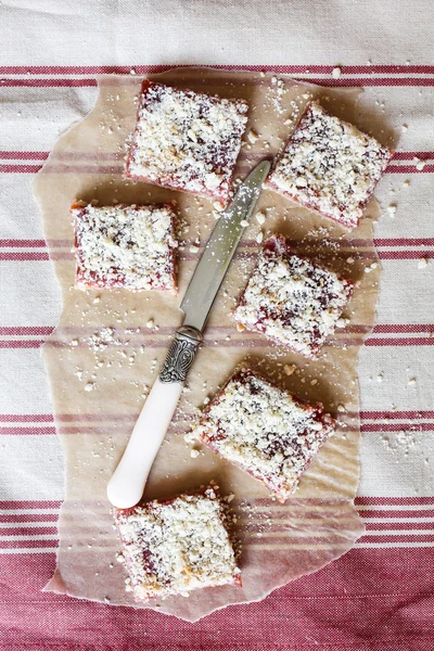 Stack of cake or cookies with plum, strawberry, raspberry and cherry jam or marmalade with sweet crumbs, cinnamon and nuts on a parchment paper, selective focus