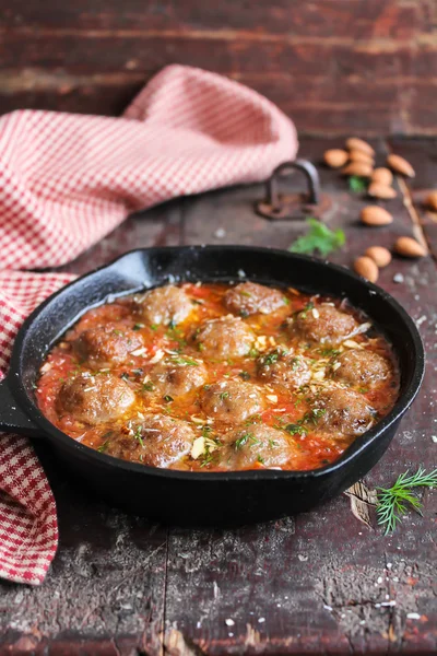 Moroccan meatballs with tomato sauce, spices, almond nuts and fresh dill in a pan on a wooden table, selective focus