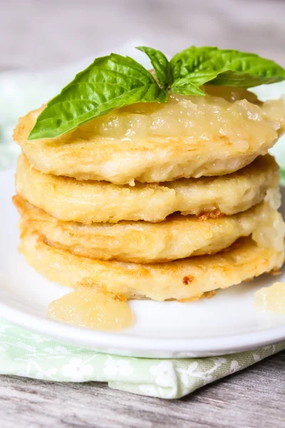 Stack of potato pancakes or fritters with apple sauce and fresh basil leaves on a plate, selective focus