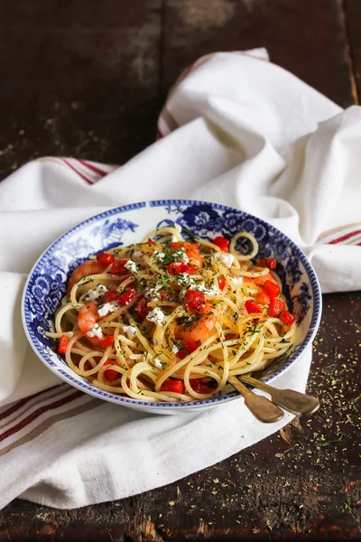 Cooked spaghetti pasta dish with roasted shrimps, chopped fresh tomatoes, red sweet pepper and salted greek feta cheese with chopped fresh dill in a bowl, selective focus