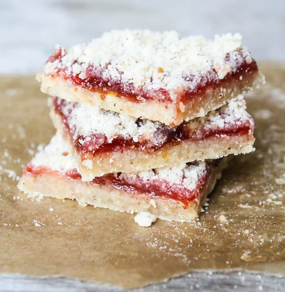 Stack of cake or cookies with plum, strawberry, raspberry and cherry jam or marmalade with sweet crumbs, cinnamon and nuts on a parchment paper, selective focus