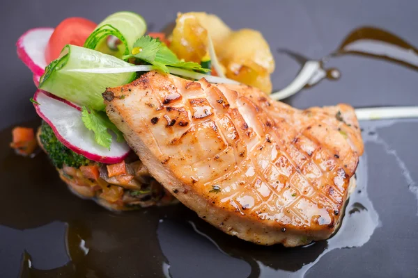 Grilled salmon fillet served with vegetable salad, radish, tomato, cucumber, apples and parsley on a plate