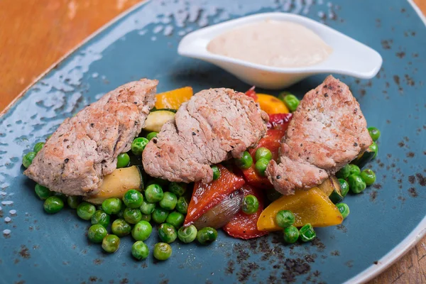 Roasted pork meat fillet chops with zucchini, onion, bell pepper, frozen peas on a plate with cream sauce