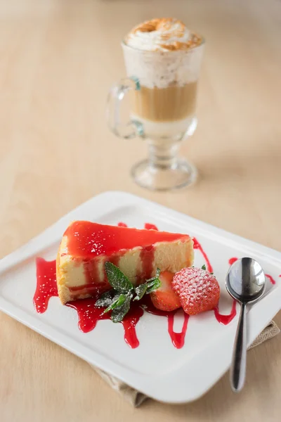 Cheesecake piece with strawberry sauce and berry, mint, icing sugar and a glass of coffee, selective focus