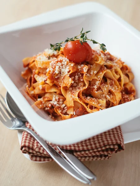 Homemade tagliatelle pasta with bolognese sauce cooked from celery, carrot, minced meat, onion and tomatoes garnished with cherry tomato and freshly grated parmesan cheese