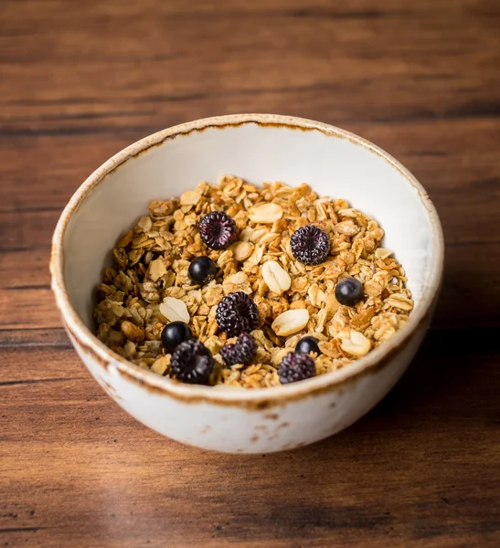 Homemade granola or muesli with oat flakes, corn flakes, dried fruits and toasted peanuts with fresh berries in a bowl for breakfast, selective focus
