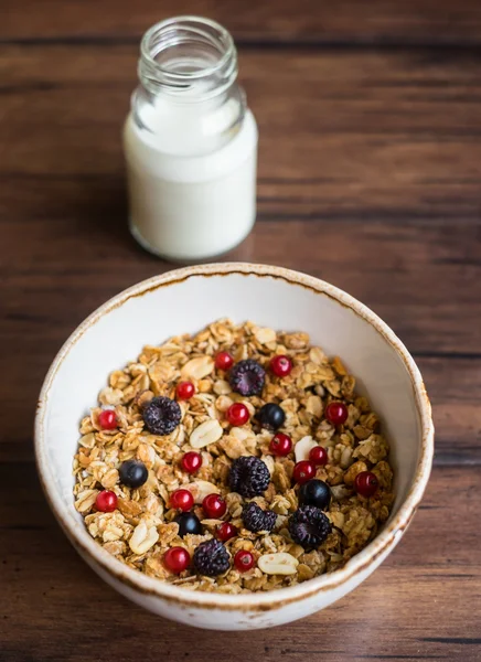 Fresh granola or muesli with toasted oat flakes, black and red currant, raspberry, blackberry, honeyed peanuts in a breakfast bowl on a wooden rustic kitchen table, selective focus