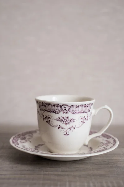 Empty clear vintage coffee cup with purple floral pattern with a dessert plate on a wooden rustic kitchen table, selective focus