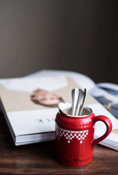 Red vintage checked milk pot and magazines on a wooden dark brown table, copy space, selective focus