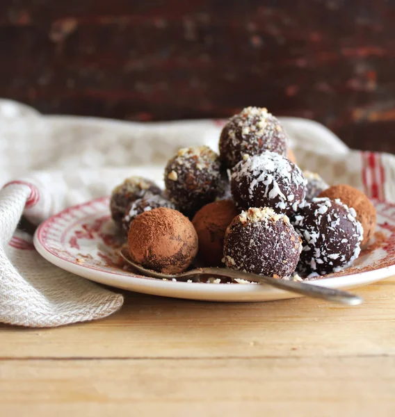 Chocolate truffles with chopped nuts, shredded coconut and cocoa powder on a dessert plate on a wooden rustic table, selective focus