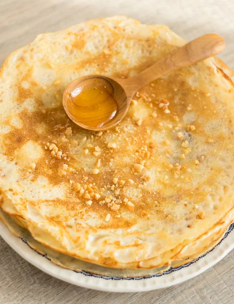 Buttermilk pancakes with honey and chopped nuts on a dessert plate on a wooden rustic kitchen table, selective focus