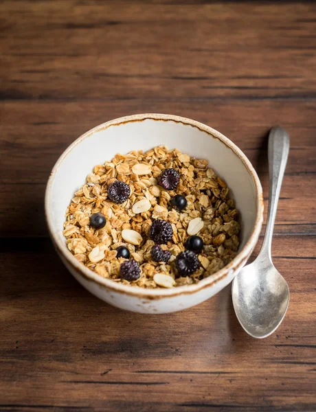 Homemade granola or muesli with oat flakes, corn flakes, dried fruits and toasted peanuts with fresh berries in a bowl for breakfast, selective focus