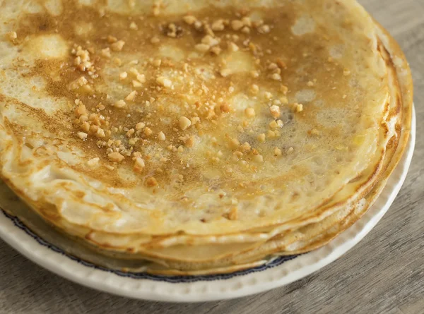 Wheat pancakes with honey and toasted nuts stacked on a dessert plate on a wooden rustic kitchen table, selective focus