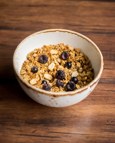 Homemade granola or muesli with oat flakes, corn flakes, dried fruits and toasted peanuts with fresh berries in a bowl for breakfast, selective focus