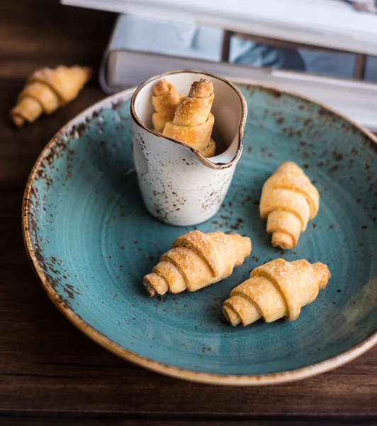 Homemade short crust pastry crescent rolls with sugar on a plate on a wooden rustic dark brown table, selective focus