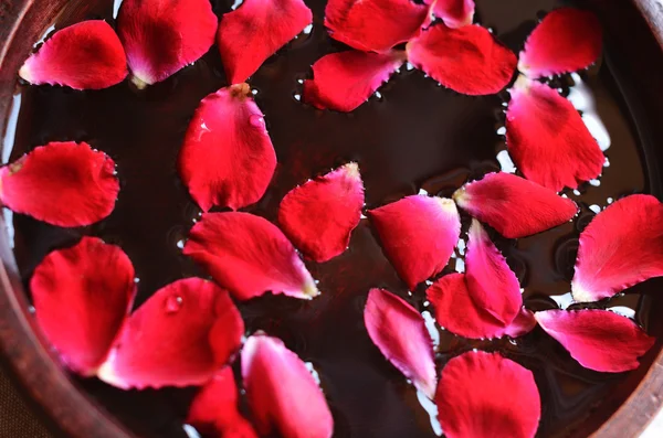 Red rose petals floating in water in wooden bowl