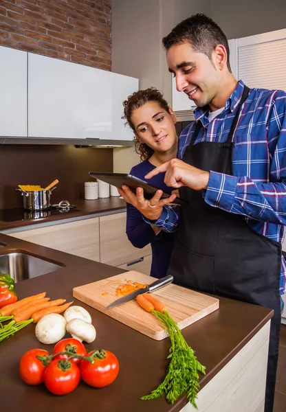 Couple in home kitchen looking recipe with a electronic tablet