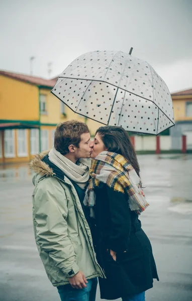 Young couple kissing outdoors under umbrella in a rainy day