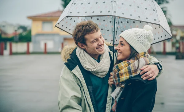 Young couple embracing and laughing outdoors under umbrella