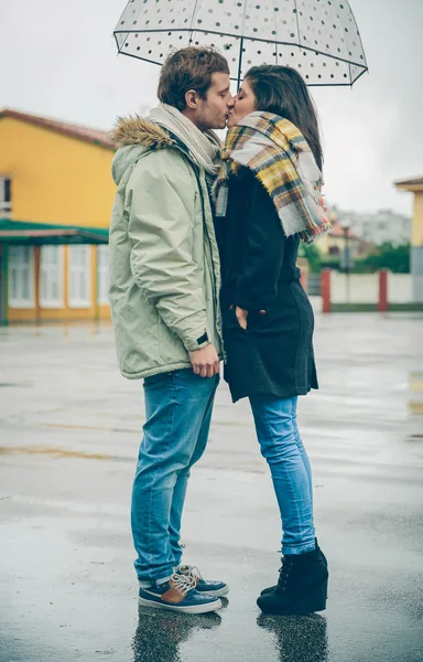 Young couple kissing outdoors under umbrella in a rainy day