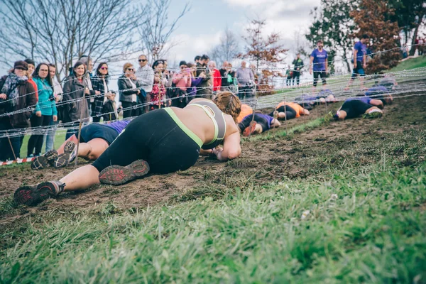 Runner crawling under barbed wire in a test of extreme obstacle race