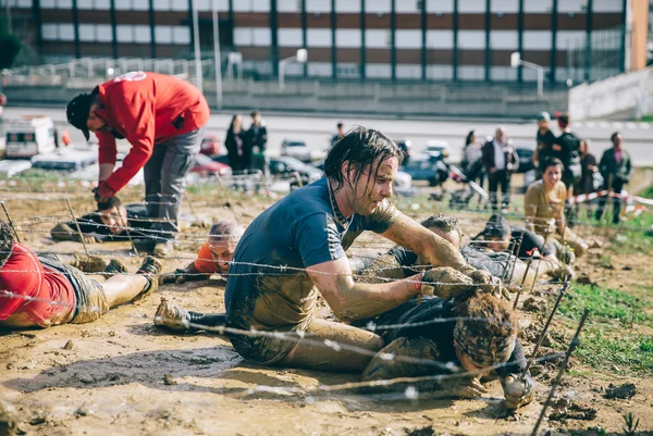 Runner helping to woman crawling under barbed wire in a test of extreme obstacle race