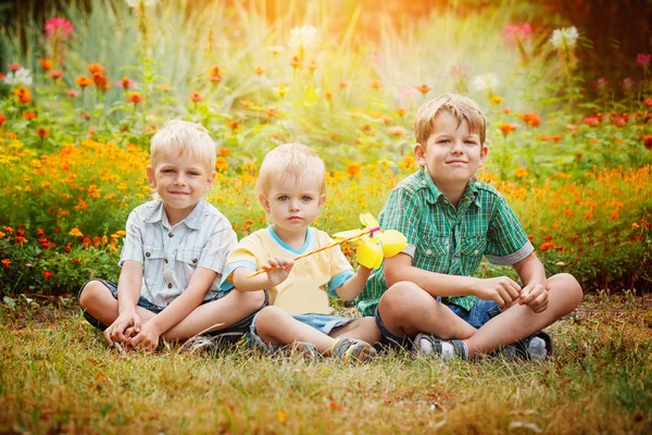 Three little brothers sitting on grass in sunny summer day.