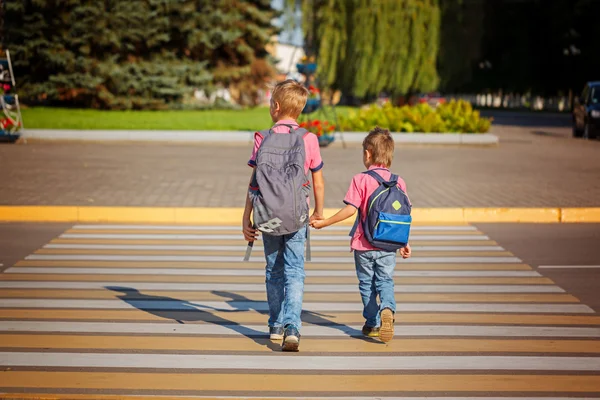 Two boys with backpack walking, holding on warm day  on the road