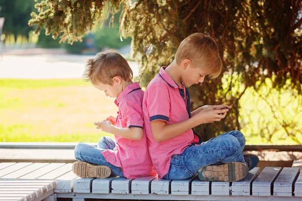 Two little boys playing games on mobile phone in sunny day, sitt