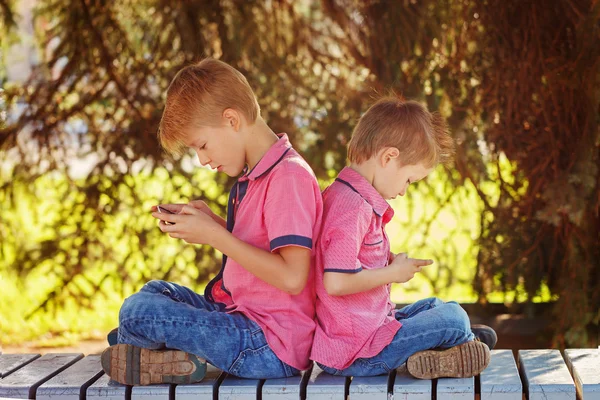 Two little boys playing games on mobile phone in sunny day, sitt