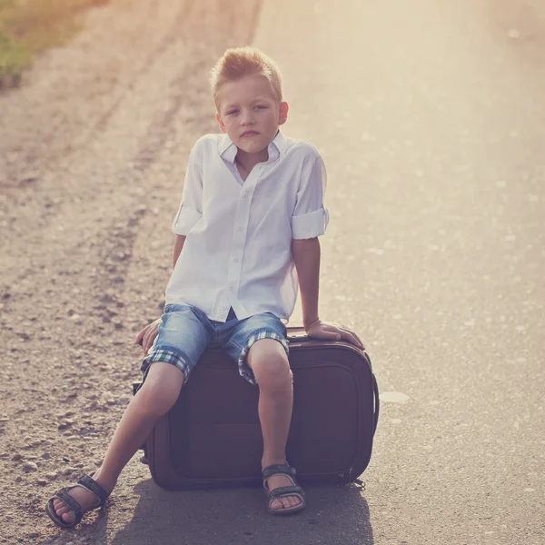 The child sits on a suitcase in the summer sunny day, the travel