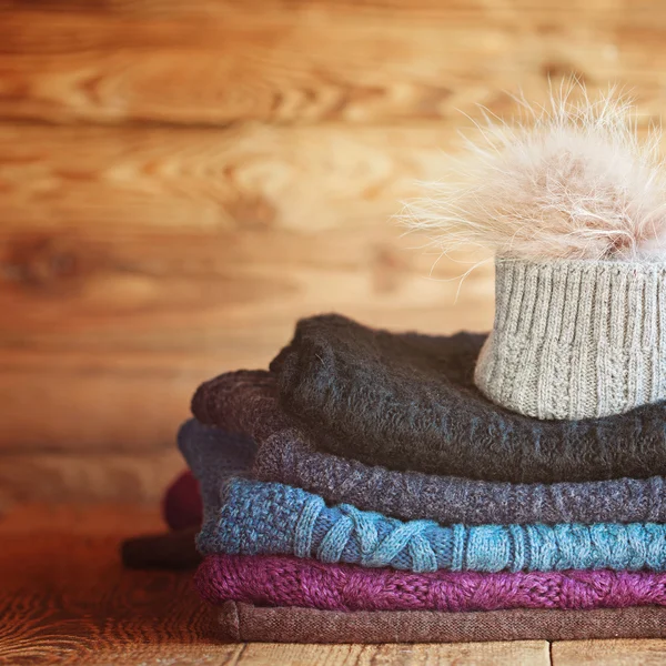 Stack of knitting colorful  warm woolen clothes on wooden wall b