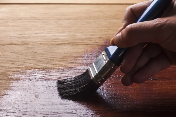 Hand holding a brush applying  varnish paint  on a wooden surface