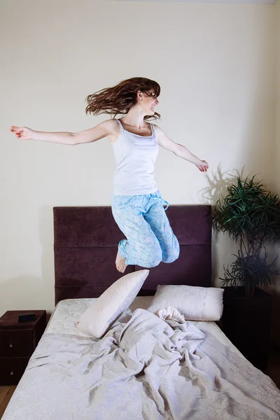 Happy young woman jumping on bed