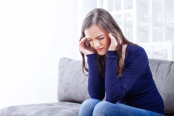 Young Woman Sitting On Sofa having headache migraine