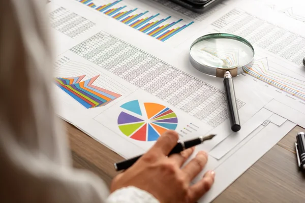 Girl and business accessories (notebook, calculator, planchette, tablet, fountain pen, glasses) and graphics, tables, charts on white sheets on office desk. Soft focus.