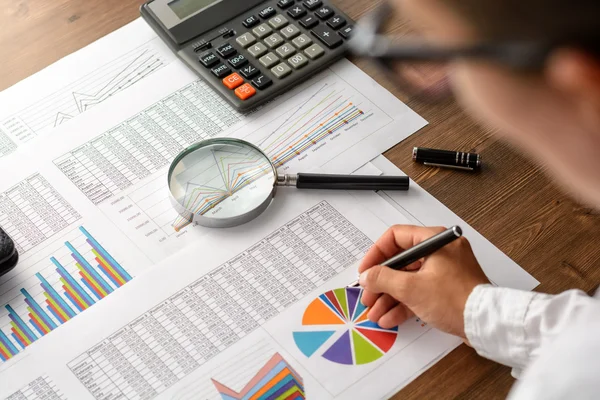 Girl and business accessories (notebook, calculator, planchette, tablet, fountain pen, glasses) and graphics, tables, charts on white sheets on office desk. Soft focus.