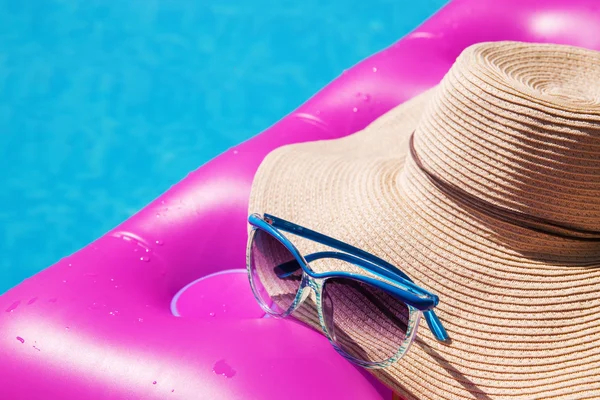 Sunglasses and straw hat pink air mattress in swimming pool