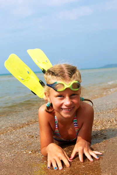 Happy little child smiling on summer beach sand with snorkel equipment looking to side at copy space after swimming with fins and mask on vacation.
