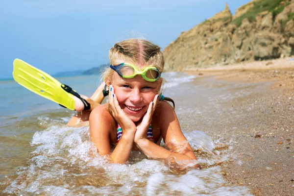 Happy little child smiling on summer beach sand with snorkel equipment looking to side at copy space after swimming with fins and mask on vacation.