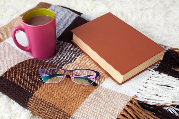 Warm knitted plaid and a book with cup on a rug