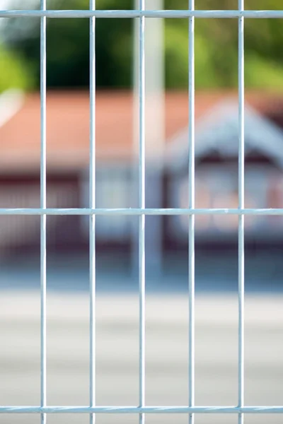 Closeup of a metal fence with blurred red house