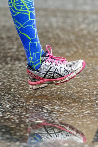 Colored running shoe with blue socks reflecting in puddle at the