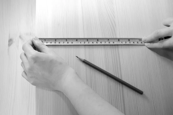 Two hands measure a wooden board with a steel tape measure