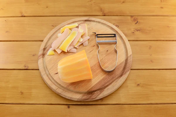 Butternut squash with a vegetable peeler on a chopping board