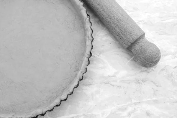 Baking tin lined with pastry, wooden rolling pin beside