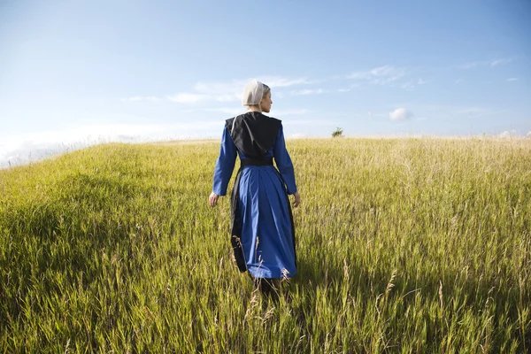 Amish woman in blue dress and black cape in field