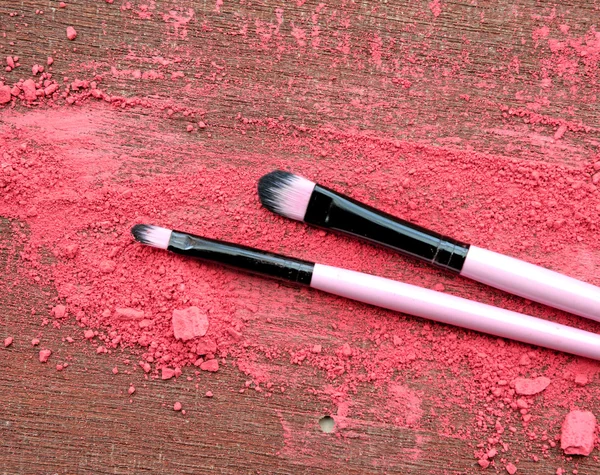 Makeup brush and crushed eyeshadows on wooden background