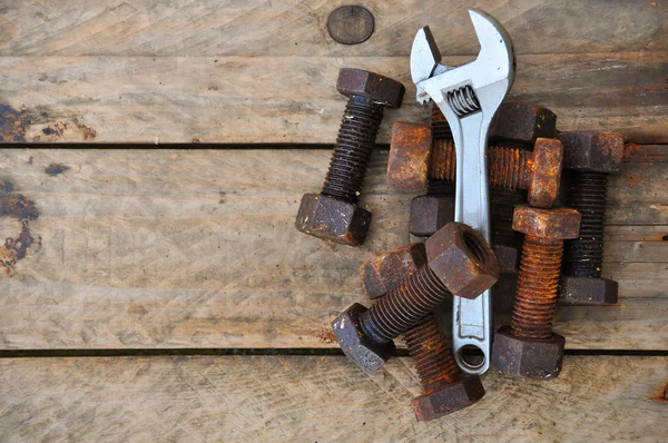 Old bolts with adjustable wrench tools on wooden background.