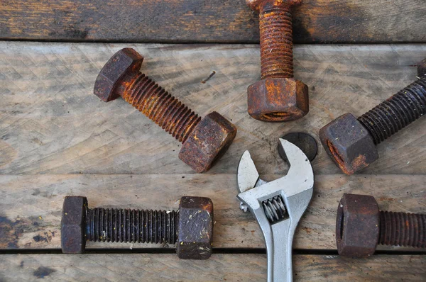 Old bolts with adjustable wrench tools on wooden background.